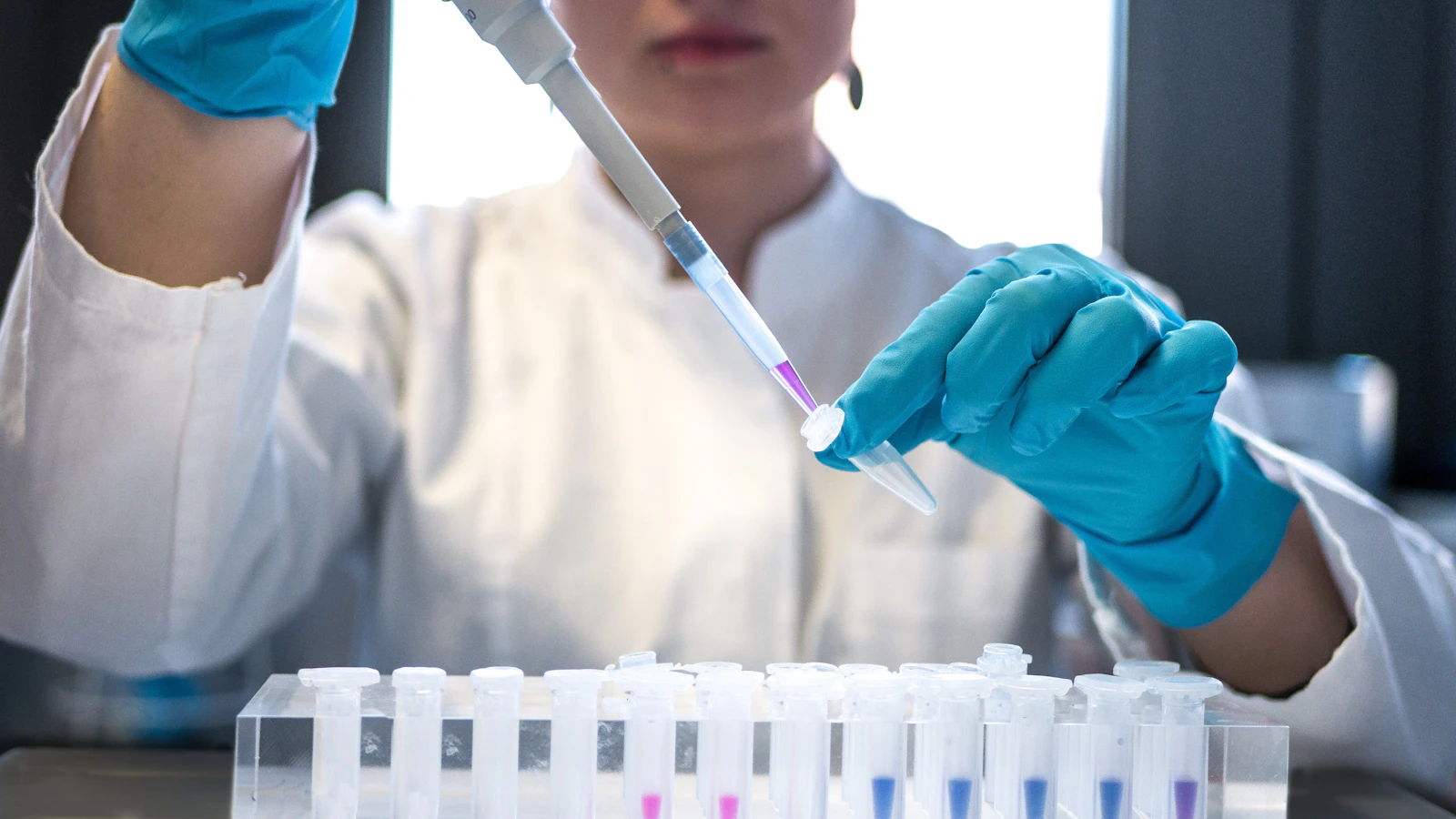 Laborant pipetteert een monster in een rij gekleurde reageerbuisjes.