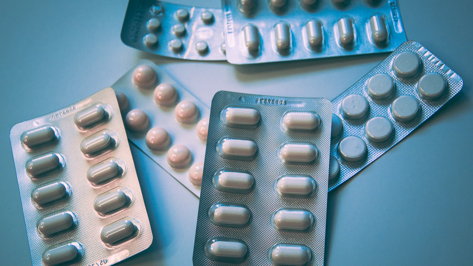 Meerdere doordrukstrips met tabletten liggen naast elkaar op een blauw oppervlak.