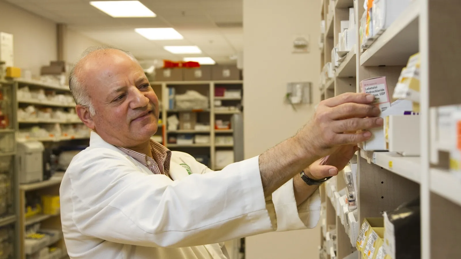 Apotheker pakt een doosje medicijnen van een schap in de apotheek.
