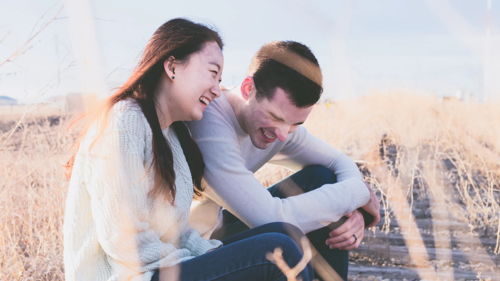 Man en vrouw zitten lachend naast elkaar in het gras op een zonnige dag.