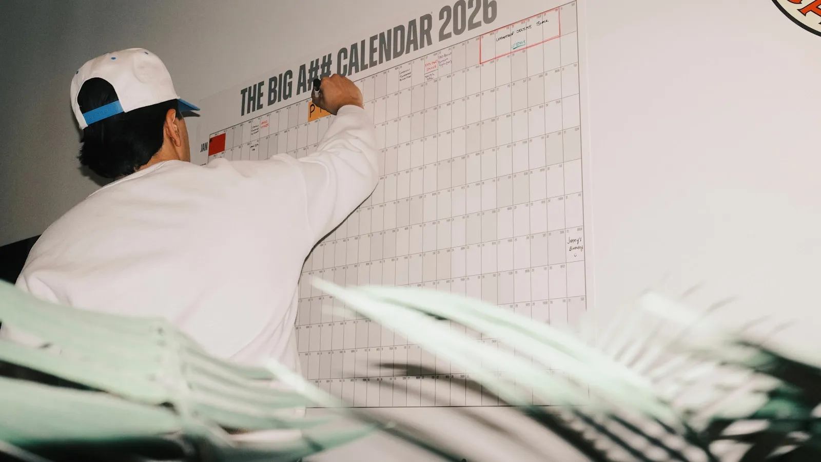 Iemand schrijft op een grote wandkalender voor 2026.