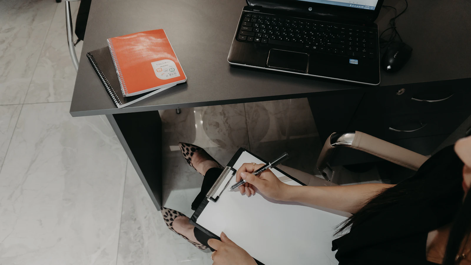 Someone filling in a checklist at a desk with a laptop.