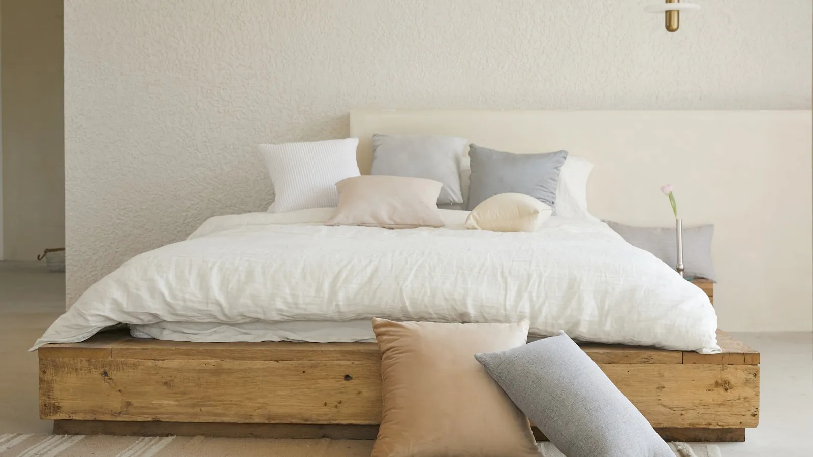 Opgemaakt bed met een wit dekbed en kussens in een lichte slaapkamer.