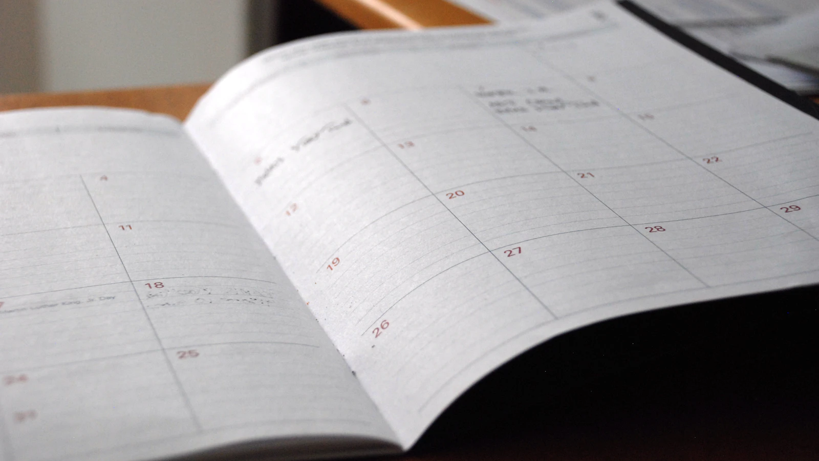 Open monthly planner with empty date boxes on a wooden desk.