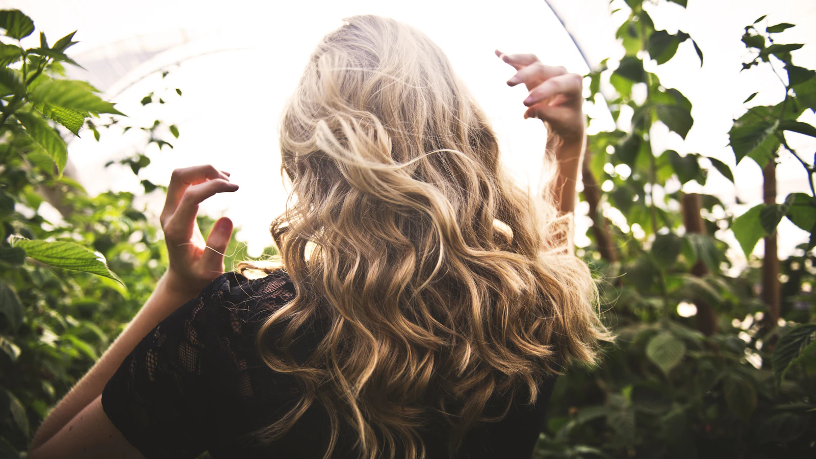 Vrouw met blond haar staat tussen hoge planten in het zonlicht.