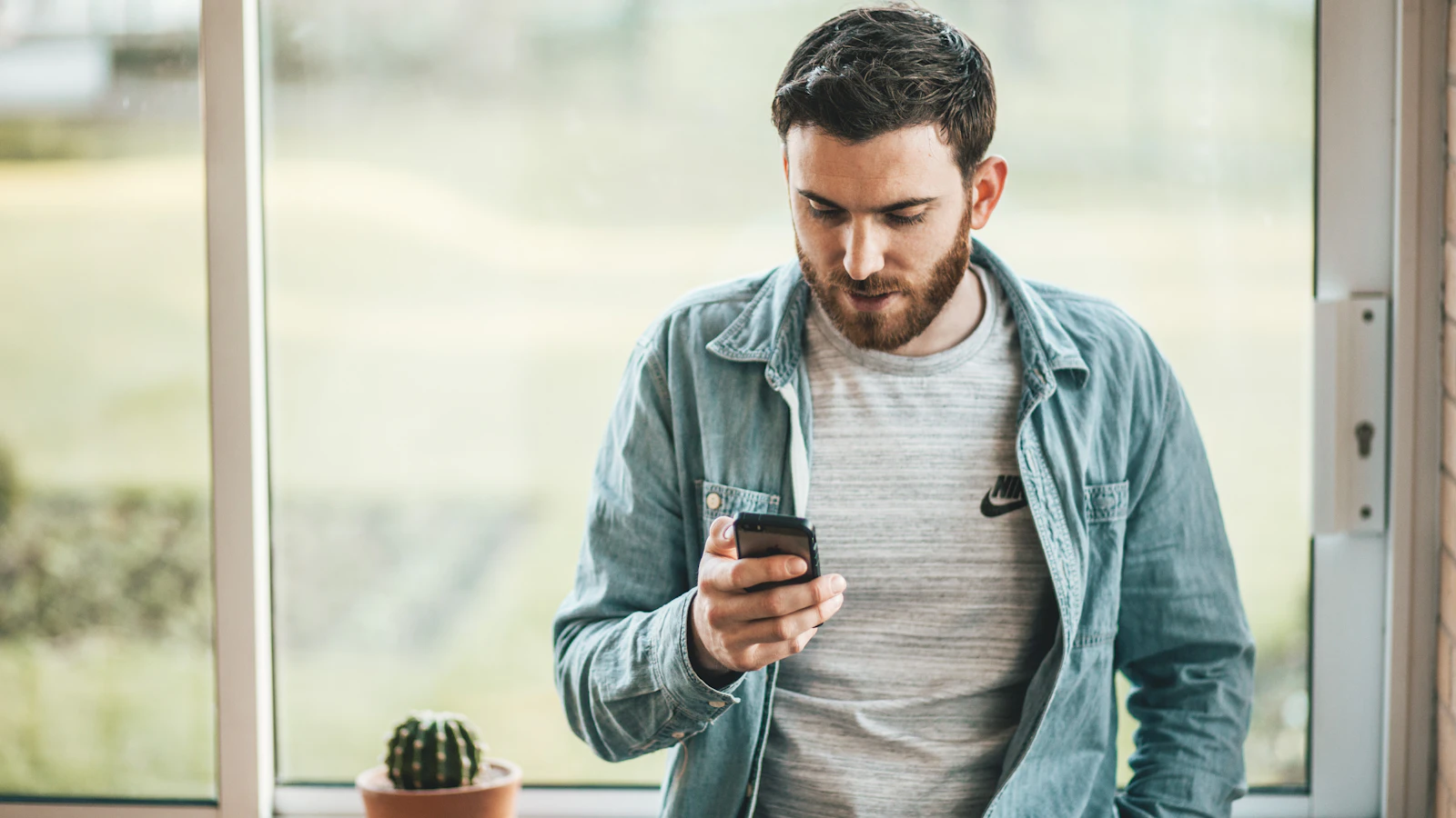 Man kijkt op zijn telefoon bij een raam met daglicht.